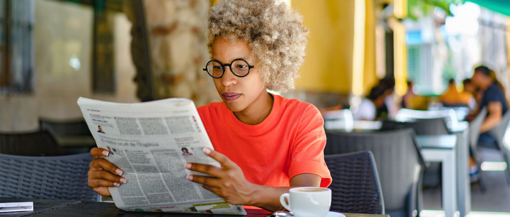 Person reading a newspaper at a café table.