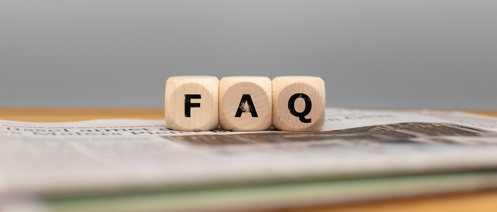 Wooden blocks spelling FAQ on top of a newspaper.