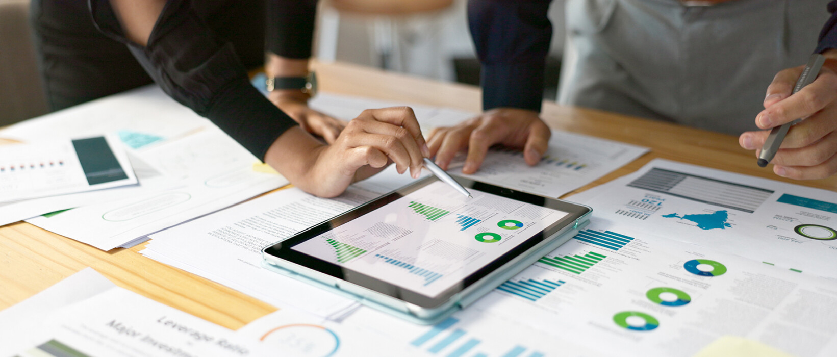 People reviewing market research charts on a tablet and printed reports.