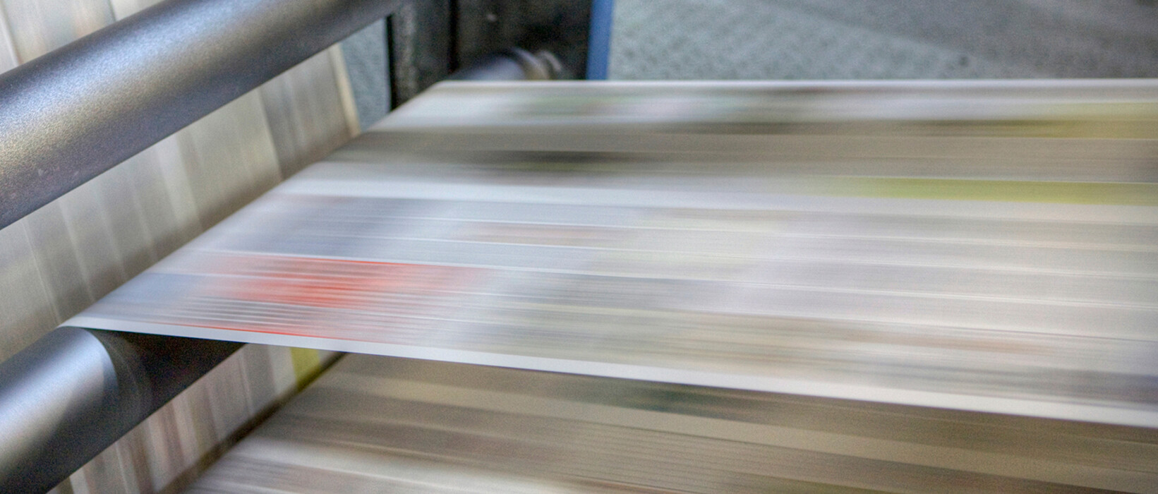 Newspapers moving through printing press rollers.