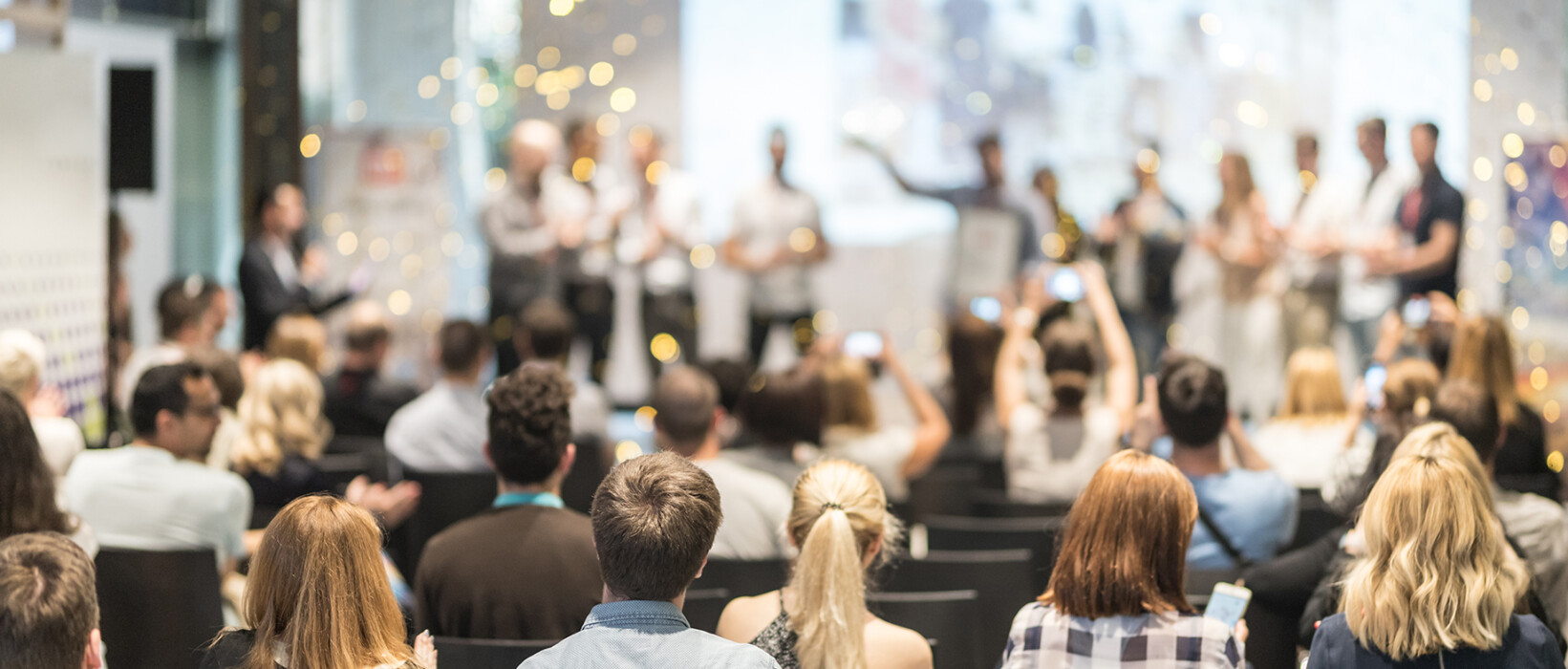 Audience attending a large event with speakers on stage.