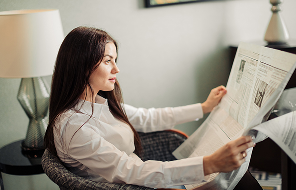 Person reading a newspaper while seated indoors.